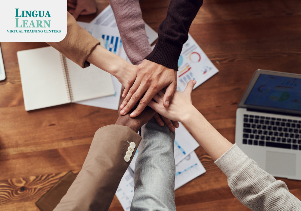 Hands of multiple people stacked together on a table with charts and a laptop